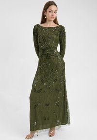 Abito da sera lungo di un verde oliva intenso con dettagli intricati di perline e ricami. Presenta maniche lunghe e una silhouette aderente, con una gonna fluida.