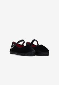 Zapatos de terciopelo negro con punta redondeada y una correa en el empeine. Presentan un interior rojo en contraste y suela de goma texturizada.