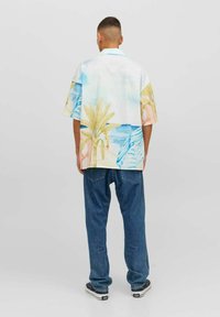 Camicia a maniche corte, con bottoni, in tessuto leggero, caratterizzata da una stampa ad acquerello di foglie di palma e oceano. Indossata con jeans blu e sneakers.