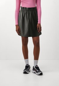 Gonna nera in ecopelle con vita elastica, abbinata a una maglietta rosa a maniche lunghe, calzettoni bianchi e scarpe da ginnastica nere.