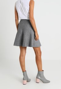 Grauer Skorts mit schwingendem Saum, kombiniert mit grauen Knöchelstiefeln mit pinken Blockabsätzen. Ein weißes ärmelloses Oberteil rundet das Outfit ab.