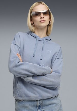Lyseblå hættejakke med frontlomme og justerbar snor. Blødt stof med en afslappet pasform. Bæres med denimjeans.