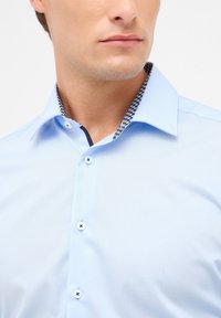 Camicia azzurra chiara con colletto strutturato e un motivo blu navy. Sei bottoni e texture di tessuto liscia.