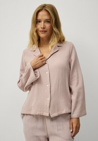 Lichtroze, knoopsluiting pyjama top van textuurstof. Heeft een kraag, lange mouwen en een ontspannen pasvorm, gecombineerd met bijpassende broek bottoms.