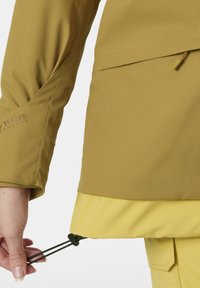 Gelbe und khakifarbene Jacke aus strukturiertem Stoff. Verfügt über einen verstellbaren Saum mit Kordelzug und ein Logodetail am Ärmel.