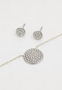 Set di gioielli in tono argento composto da orecchini a bottone rotondi e un bracciale abbinato, entrambi decorati con strass trasparenti in un'impostazione pavé.