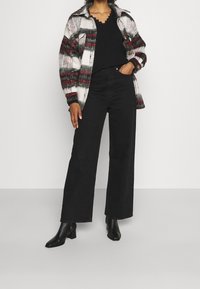 Rutig knäppjacka i vitt, svart och rött, tillsammans med en svart strukturerad stickad tröja och vida svarta jeans. Svarta klackstövlar.