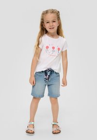Weißes Baumwoll-T-Shirt mit pinkem Flamingo-Graphic und Text, kombiniert mit Jeans-Shorts und einem gemusterten Gürtel. Sandalen mit verstellbaren Riemen.