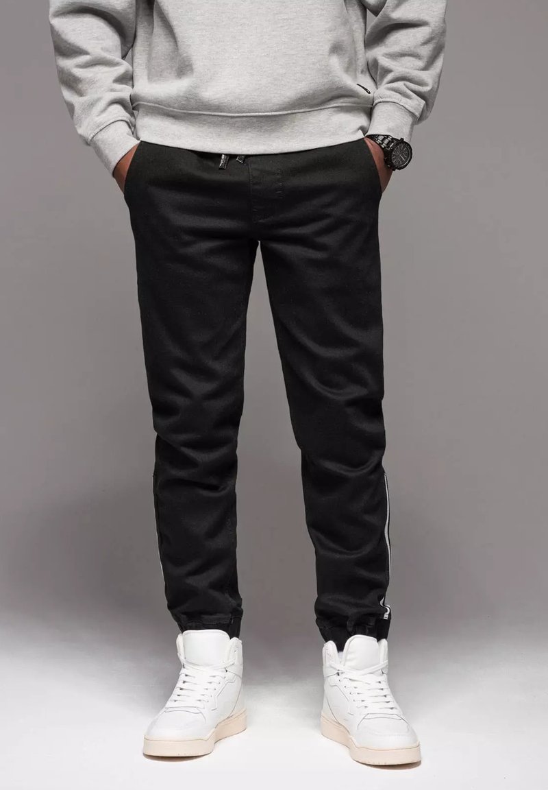 Czarne joggery o slim fit, z zamkiem błyskawicznym i białym paskiem po bokach. W połączeniu z białymi sneakersami typu high-top.