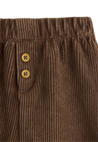 Brune corduroypants med lodrette striber, der har en strækbar talje og to gule knapper foran. Blødt, tekstureret stof.