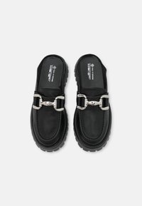Sorte slip-on sko lavet af læder med en gummisål, der har en sølv spænde detalje og syninger langs kanterne.