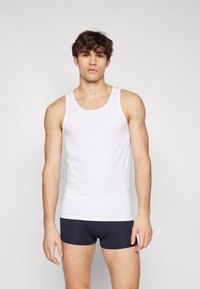 Débardeur en coton blanc avec de larges bretelles, associé à un short boxeur bleu marine. Texture douce, design ajusté, style minimaliste.