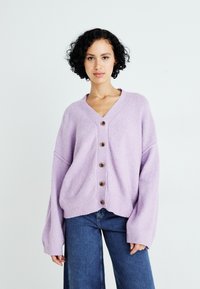 Cardigan lavorato a maglia di un leggero colore viola, con collo a V, sei bottoni in legno e polsini a coste, abbinato a jeans a gamba larga blu.