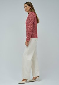Roter, gestrickter Pullover mit lockerem Gewebe, rundem Halsausschnitt und langen Ärmeln, kombiniert mit weißen, weit geschnittenen Hosen und beigen Absatzschuhen.