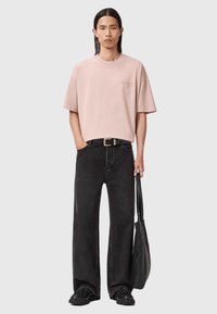 Jasnoróżowa, oversize'owa koszulka z krótkim rękawem, ciemne szerokie dżinsy oraz czarne buty. Akcesoria obejmują fakturowaną czarną torbę na ramię.