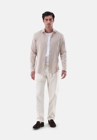 Camicia button-down beige chiaro con colletto, abbinata a pantaloni color crema e mocassini marrone scuro. Design semplice con una vestibilità comoda.