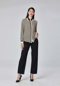 Blouse à manches longues et boutons en crème avec un motif de nid d'abeille noir, associée à un pantalon droit en denim foncé et des escarpins noirs à talons aiguilles.