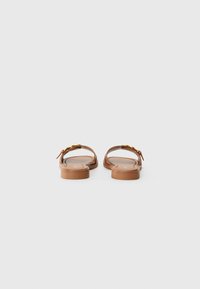 Sandales en cuir marron à semelle plate, avec un design de bride simple et un accent doré sur le dessus.