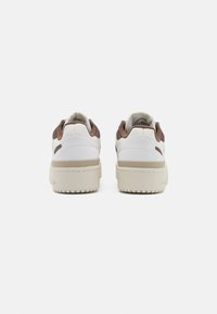 White sneakers with a textured brown accent at the heel, featuring a thick cream sole and smooth leather material. Minimalist design.
