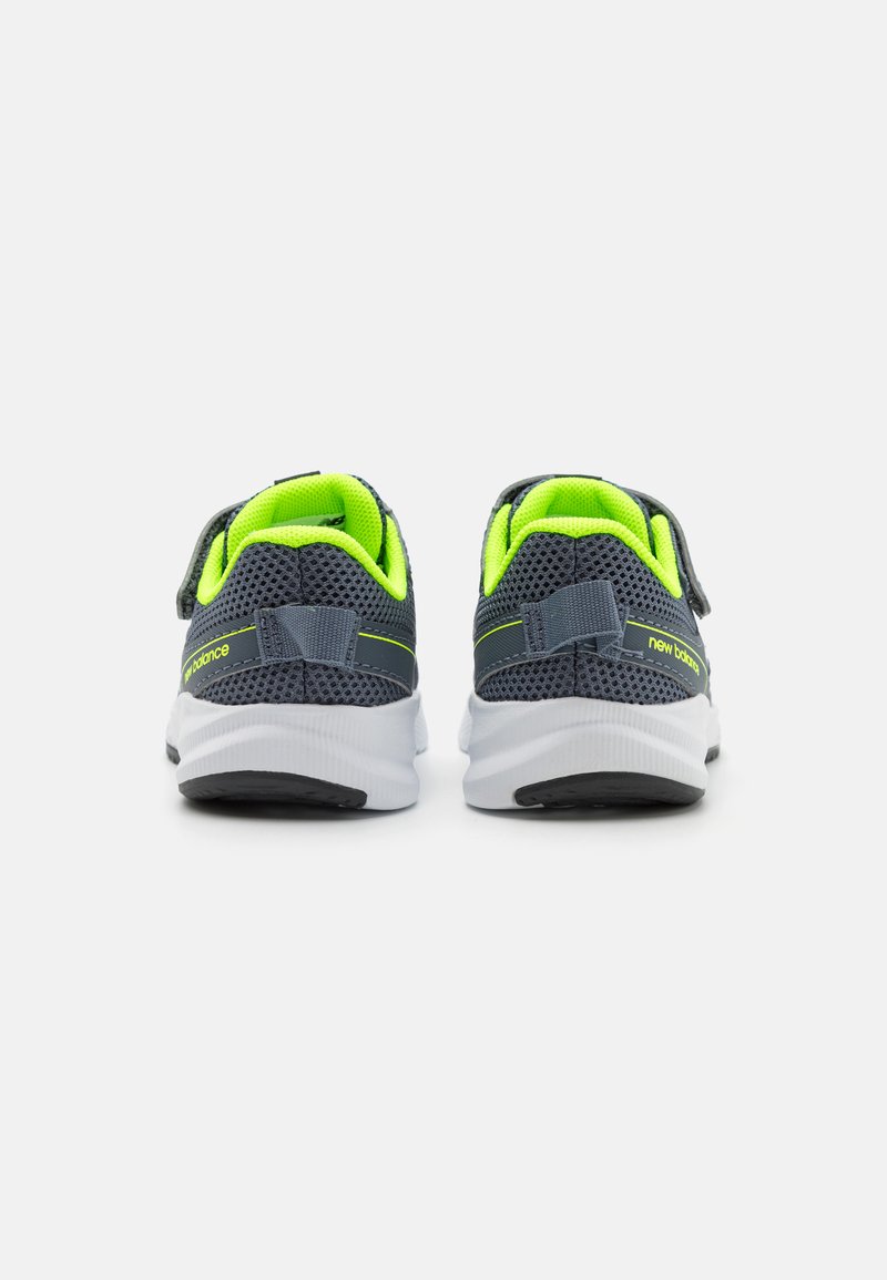 Baskets de sport grises avec des accents verts, tige en mesh et sangle ajustable. Semelle blanche épaisse avec un cuir noir. La vue arrière montre des coutures détaillées.