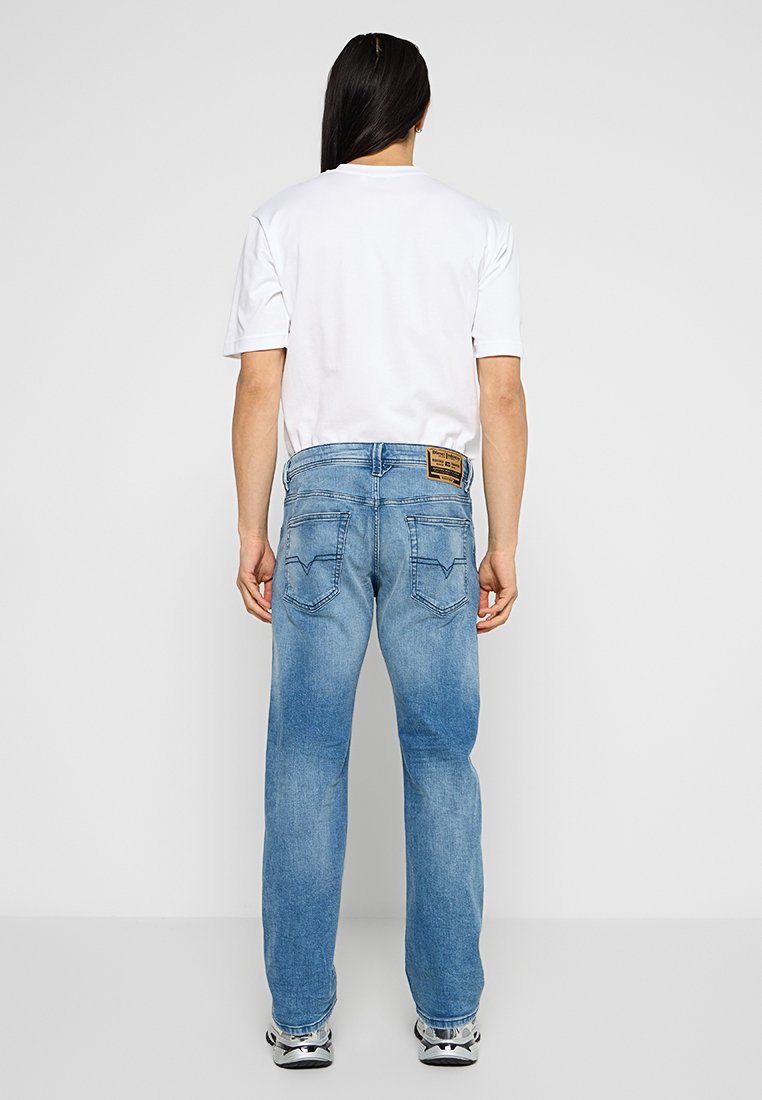 Helle blaue Jeans aus Denim mit geradem Bein, mit Gesäßtaschen und einem Etikett am Bund, kombiniert mit einem weißen T-Shirt.