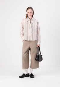 Stripet lyserød og kremfarget skjorte med knapper, beige vidbukser, svarte loafers, hvite sokker og en liten svart håndveske.