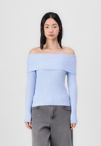 Lyseblå, ribbet off-the-shoulder sweater med lange ærmer, tætsiddende design og struktureret overflade, parret med grå bukser.