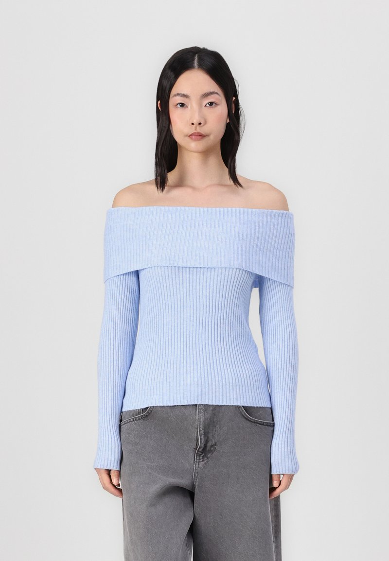 Lyseblå, ribbet off-the-shoulder sweater med lange ærmer, tætsiddende design og struktureret overflade, parret med grå bukser.