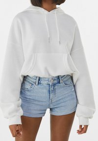 Vit hoodie med känguruficka, huva med dragsko och ribbade muddar, kombinerad med ljusblå jeansshorts med sliten finish.