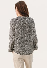 Zwart-witte bloemenblouse met lange mouwen, een losse pasvorm en een ronde halslijn. De stof lijkt lichtgewicht met een zachte textuur.