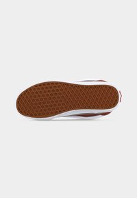 Semelle de chaussure avec un motif gaufre marron, une semelle intermédiaire blanche et une tige rouge et blanche visible de côté, isolée sur un fond clair.