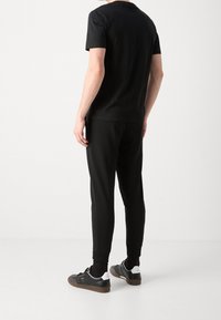 Camiseta de algodón negra de manga corta, combinada con pantalones jogger negros y zapatillas negras con acentos blancos. Diseño simple, sin patrones.