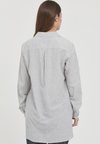 Camicia a maniche lunghe con un motivo a righe verticali in grigio e bianco, con colletto e dettaglio plissettato sul retro.