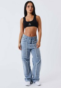 Top corto nero con logo, pantaloni cargo in denim leggeri a vita alta di colore blu chiaro con design a patchwork e orli sfrangiati, abbinati a sneakers bianche.