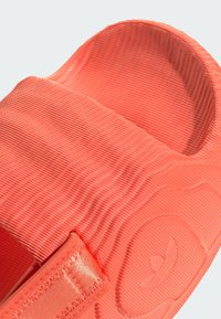 Coral-colored slide with textured ribbed surface and smooth strap. Features a logo and stitched accents for secure fit.