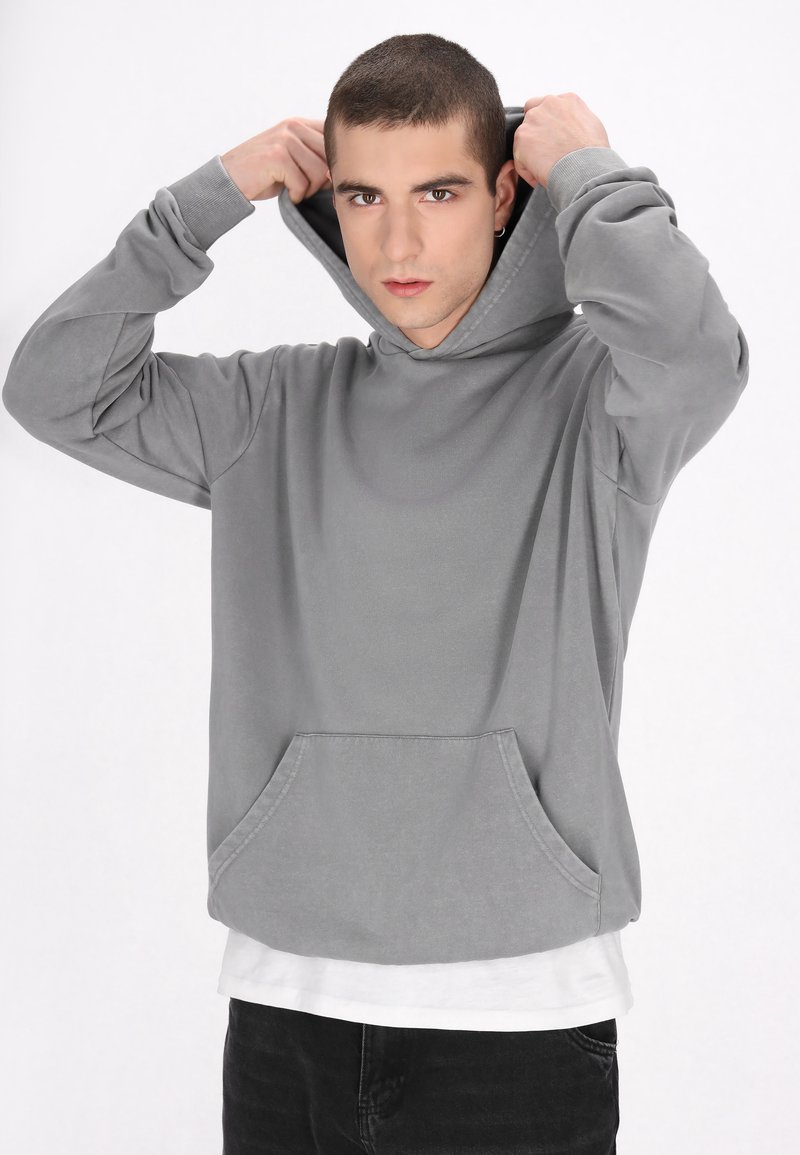 Szürke kapucnis pulóver elülső zsebből, hosszú ujjakból és laza szabásból áll. Az anyag lágyan sima tapintású.