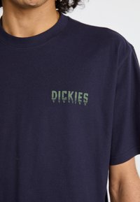 Jūrinės medvilnės marškinėliai su mažu žaliu logotipu „DICKIES“ kairėje krūtinės pusėje. Trumpomis rankovėmis ir apvaliu kaklu.