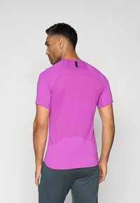 T-shirt de sport à manches courtes en rose vif, fabriqué en tissu respirant avec une finition texturée, comportant un détail en boucle noire à l'arrière et des coutures plates.