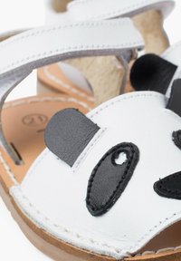 Sandale blanche avec accents noirs de visage de panda, en cuir, présentant une tige texturée et un design ouvert avec des sangles ajustables.