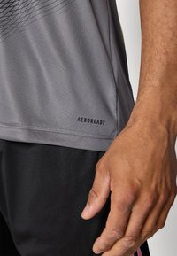 Gray athletic shirt with subtle horizontal lines, Aeroready logo at hem, paired with black shorts, showcasing a smooth, moisture-wicking fabric.