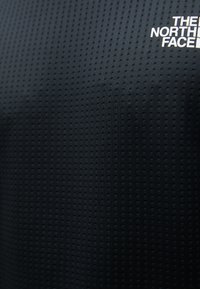 Schwarzer technischer Stoff mit perforierter Textur. Auffälliges weißes Logo in der oberen linken Ecke. Nahaufnahme des Materials.