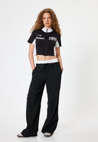 Zwart-wit cropped zip-up top met logo print, gecombineerd met losse zwarte broek met elastische tailleband en trekkoord.