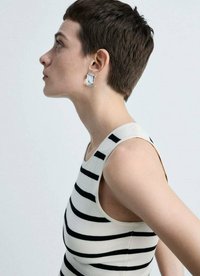 Strieborné náušnice abstraktného tvaru, hladký povrch, nosené na krátkych vlasoch. Modelka má na sebe pruhované bezrámové tričko v čiernej a krémovej farbe.