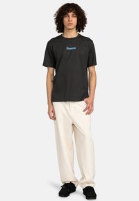 Sort t-shirt med korte ærmer med "Element" logo i blå, sammen med løstsiddende bukser i cremefarve og sorte sneakers.