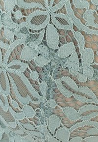 La tela de encaje presenta intrincados patrones florales en un suave color verde menta, con una textura delicada y áreas transl�úcidas que revelan una ligera capa inferior.