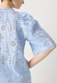Lichtblauw blouse met bloemenoeiletten borduurwerk, golvende mouwen en textuurstof. Heeft een ronde halslijn en een losse pasvorm.