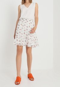 White sleeveless blouse with V-neck paired with a floral print mini skirt featuring ruffled hem, accented by orange suede slip-on sandals.