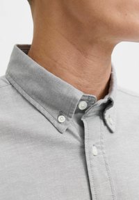 Camicia grigia con bottoni, caratterizzata da un colletto slim, bottoni bianchi e un tessuto texturizzato con cuciture visibili lungo la patta e il colletto.