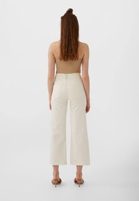 Kermankukaiset leveälahkeiset housut, joissa on korkea vyötärö, sahattu helma ja kaksi takataskua. Yhdistetty istuvaan ruskeaan toppiin ja remmi korkokenkiin.