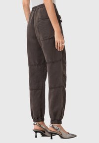 Pantaloni marrone scuro, a vestibilità comoda, con vita e polsini elasticizzati. Presentano tasche laterali e una finitura testurizzata. Abbinati a tacchi a slingback argentati.